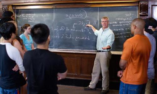 Students in classroom in front of chalk board listening to faculty member.